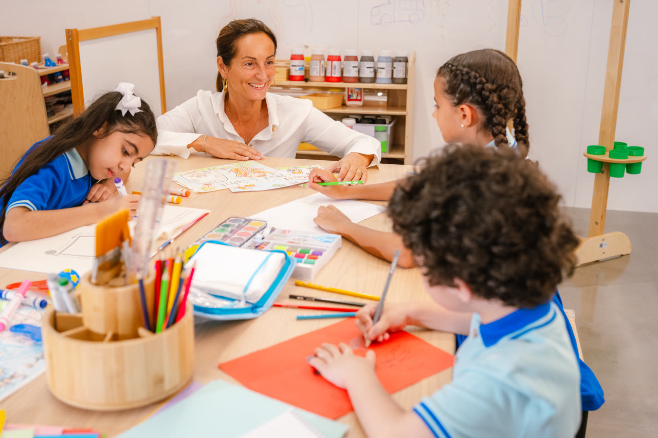 An adult works with learners around an art table.